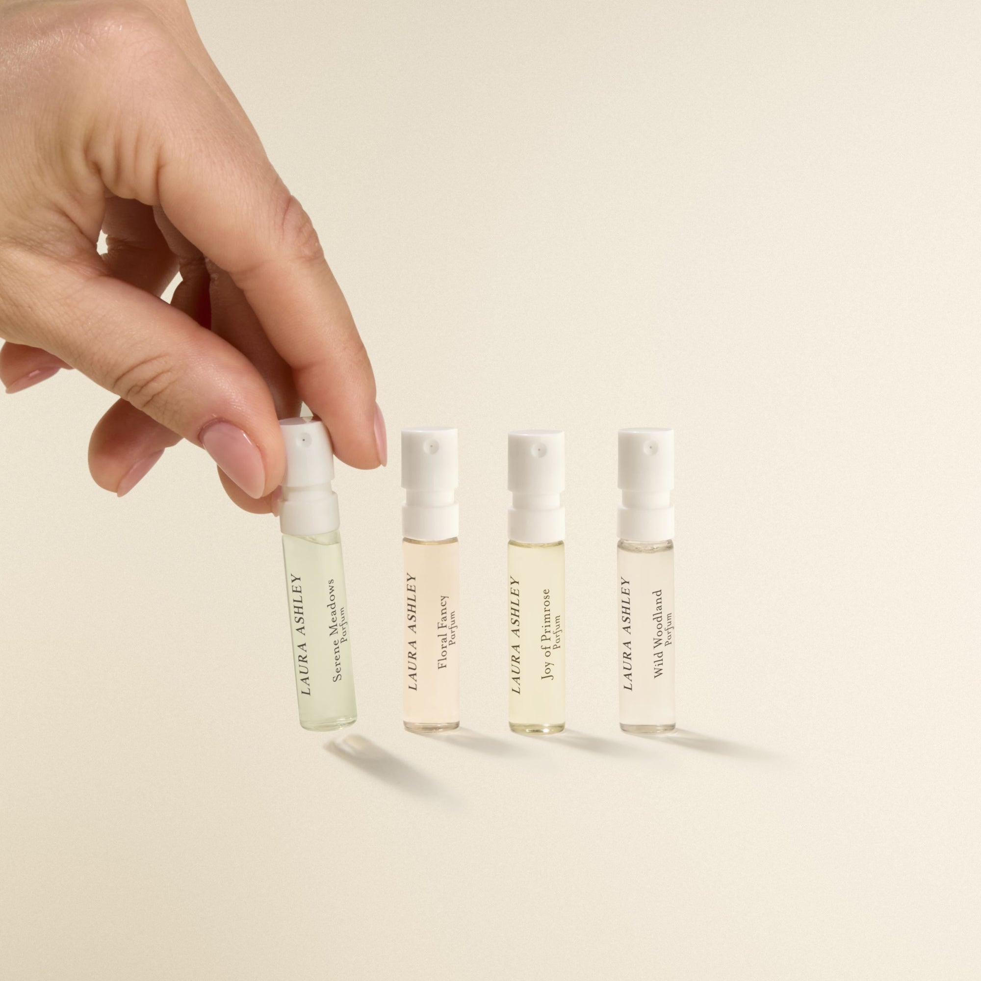 Hand holding a small bottle of Laura Ashley perfume with other bottles in the background on a beige background