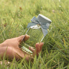 Hand holding a Laura Ashley Serene Meadows Perfume bottle with a blue ribbon in a grassy field