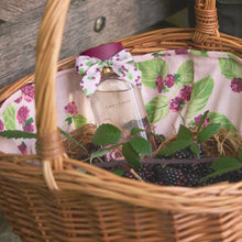 Wicker basket with a floral liner containing a bottle of Laura Ashley perfume and blackberries.